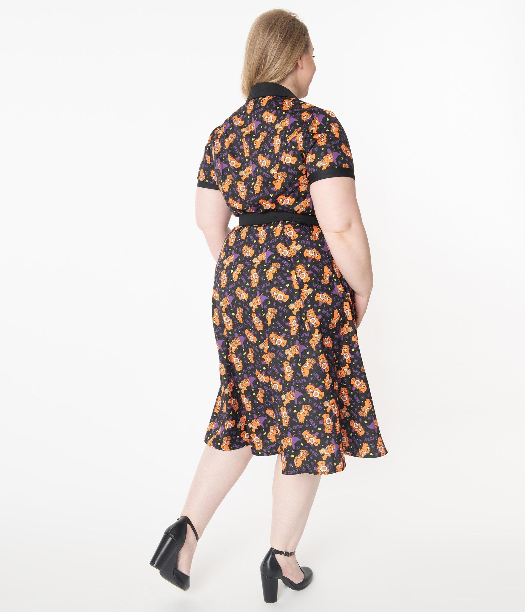 This is a Care Bears Halloween Creepy black swing dress from Unique Vintage and it has an orange trick-r-treat bear with a pumpkin, black belt, black collar and the plus model has blonde hair pulled to the side and is wearing black shoes.