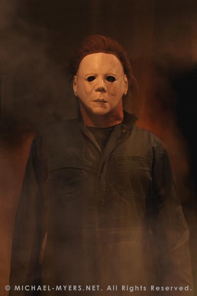 This is a Halloween II Michael Myers mask, that is a white face with brown hair and eye holes and green coveralls.