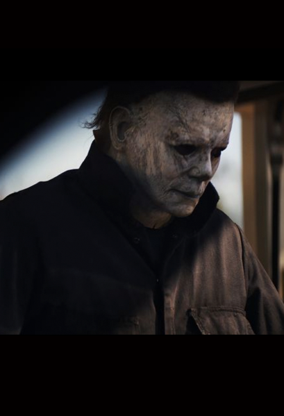 This is a Halloween 2018 Michael Myers movie still with a mask that is weathered grey face and he is wearing grey coveralls.