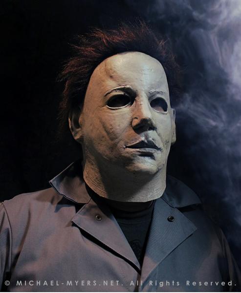 This is a Halloween 6 Curse of Michael Myers mask that is white with brown hair and black eyes and he is wearing coveralls.