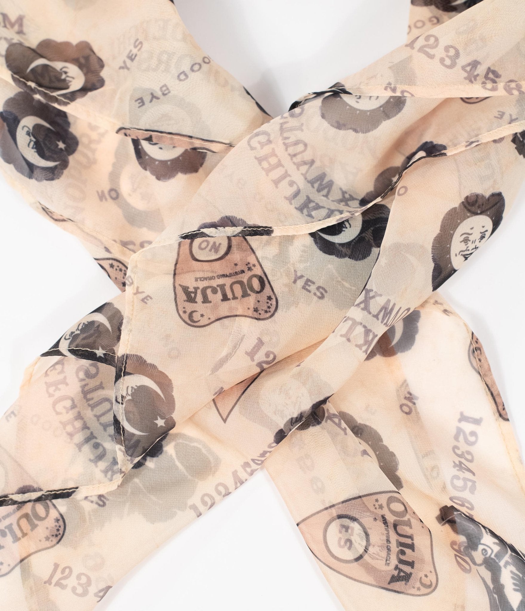 This is a Ouija chiffon hair scarf that is tan with black moons and brown planchettes.