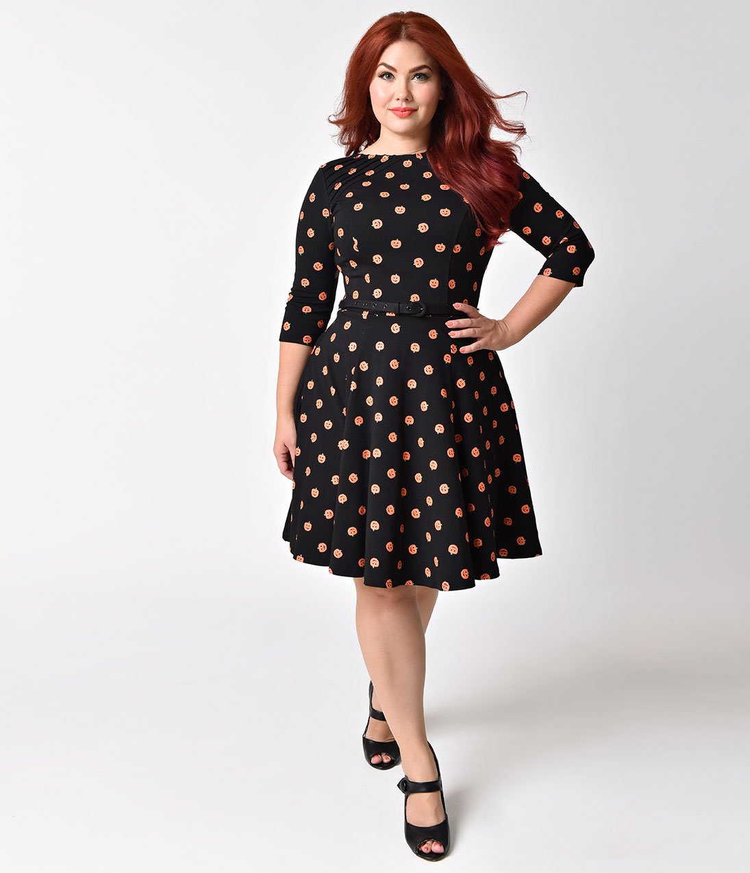 This is a black pinup flare dress with orange pumpkins and 3/4 sleeves and the plus model is wearing black shoes and has red hair.
