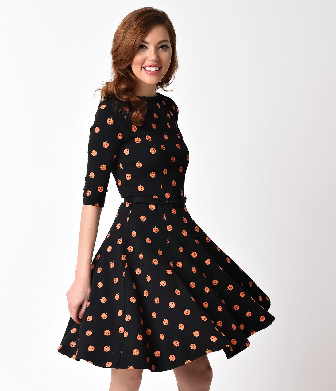 This is a black pinup flare dress with orange pumpkins, belt and 3/4 sleeves and the model is wearing black shoes and has brown hair. and is spinning.