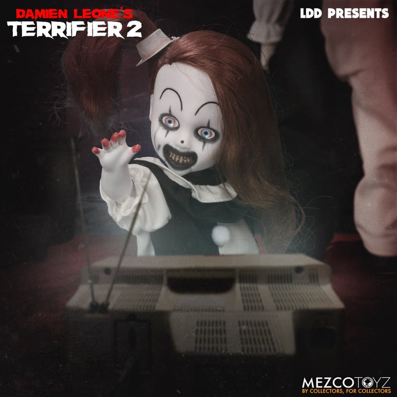 This is a little pale girl clown from the movie Terrifier 2 and she has a white face, white hat, black and white dress, bloody fingers  and blue eyes