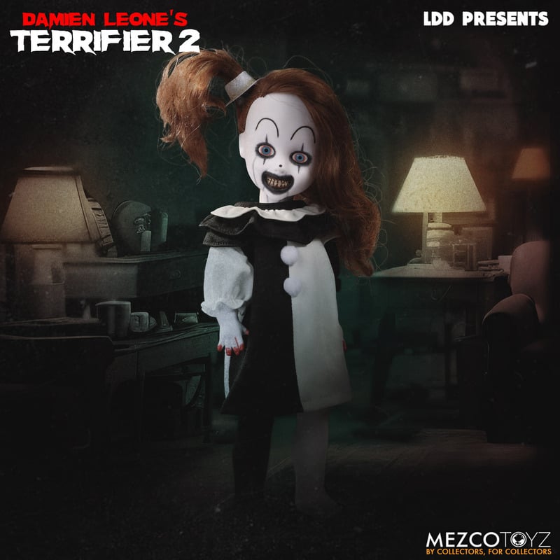 This is a little pale girl clown from the movie Terrifier 2 and she has a white face, white hat, black and white dress and blue eyes