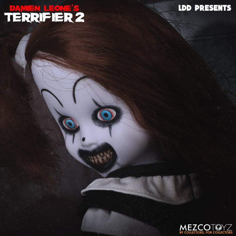 This is a little pale girl clown Living Dead Doll from the movie Terrifier 2 and she has a white face, brown hair and blue eyes