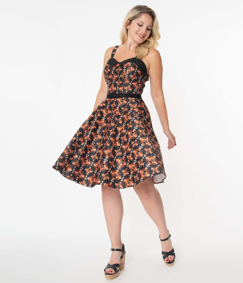 This is a Unique Vintage Halloween Rachel swing dress that has black cats, bats and skulls with orange print and the model is wearing black shoes.
