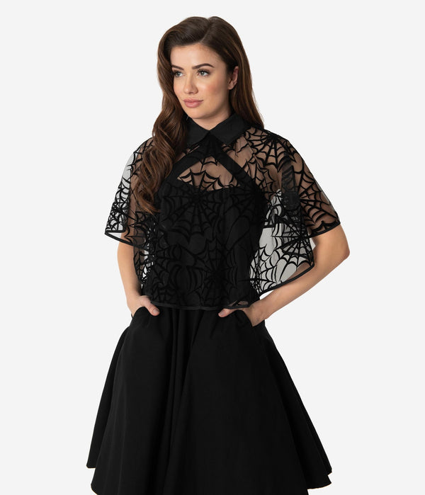 This is a black spiderweb cape, that is worn with a black dress with pockets and the model has dark hair.