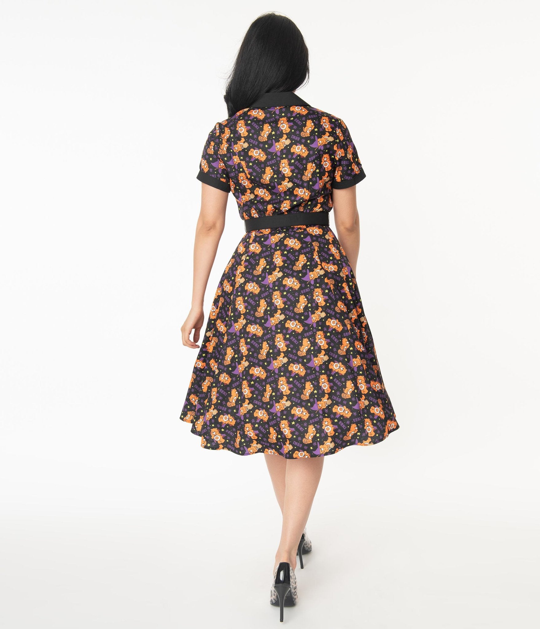 This is a Care Bears Halloween Creepy black swing dress from Unique Vintage and it has an orange bear with a pumpkin and the model has black hair pulled to the side and is wearing leopard print shoes. 