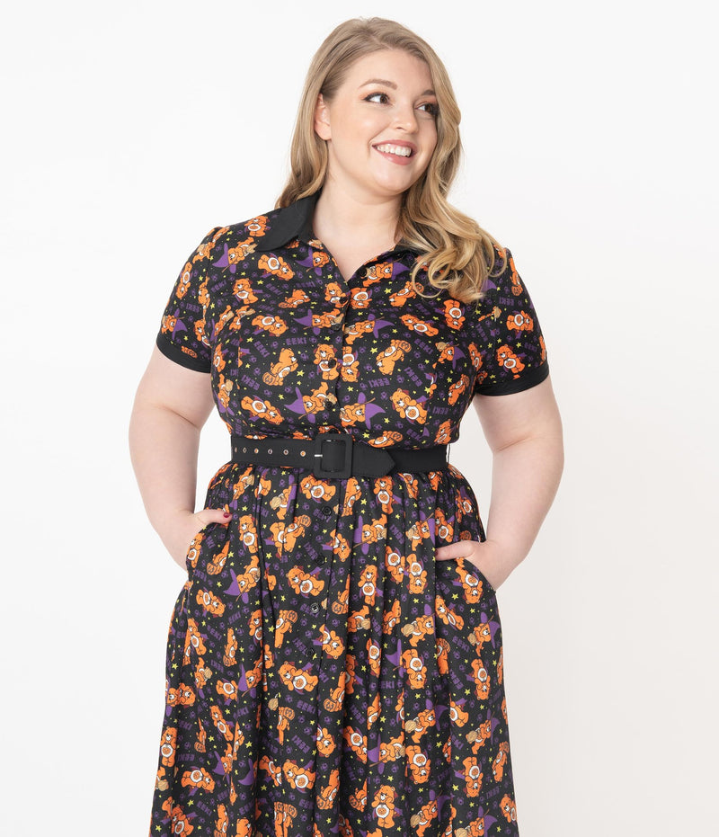 This is a Care Bears Halloween Creepy black swing dress from Unique Vintage and it has an orange trick-r-treat bear with a pumpkin, black belt, black collar and the plus model has blonde hair and is wearing black shoes and her hands are in the pockets. 