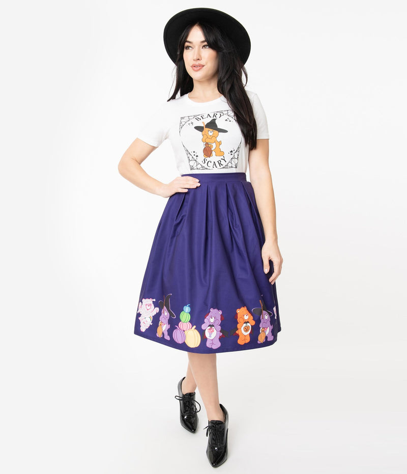 This is a Care Bears halloween purple Jayne swing skirt by Unique Vintage and the model is wearing a white shirt and has on black shoes and a black hat and her hand is on her hip.