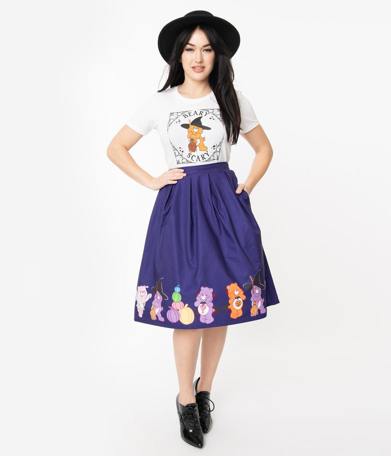 This is a Care Bears halloween purple Jayne swing skirt by Unique Vintage and the model is wearing a white shirt and has on black shoes and a black hat and her hands are on her hip and in her pocket.