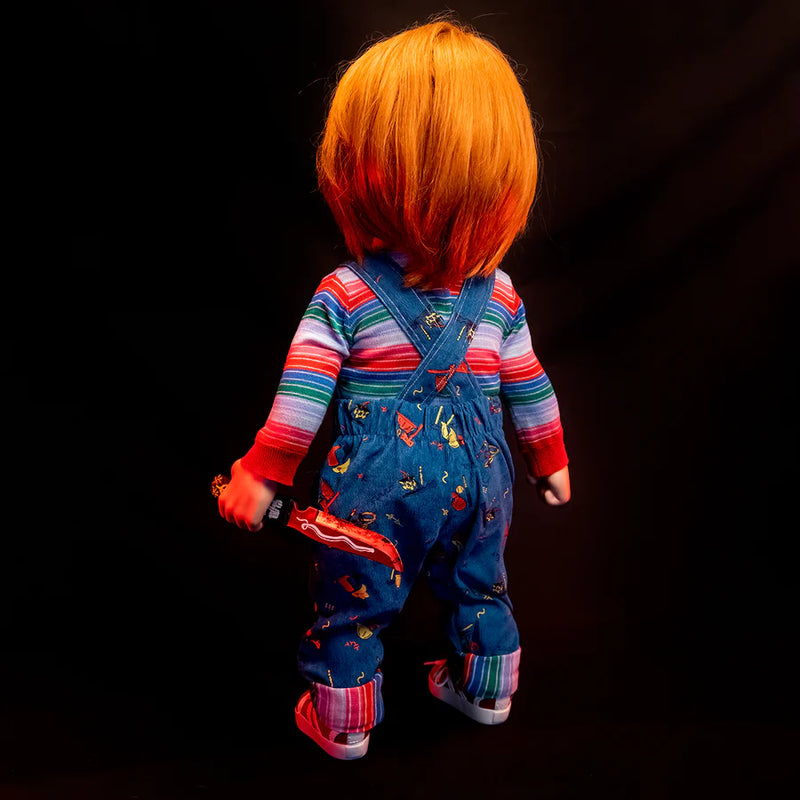 This is a Child's Play 2 Ultimate Chucky doll and he is wearing blue jean overalls, a striped long sleeve shirt, red shoes and he has orange hair
