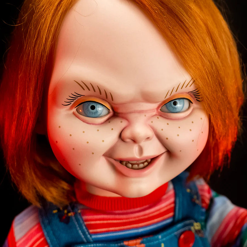 This is a Child's Play 2 Ultimate Chucky doll and he is wearing blue jean overalls, a striped long sleeve shirt, red shoes and he has orange hair and his face is crunched up like he is mad