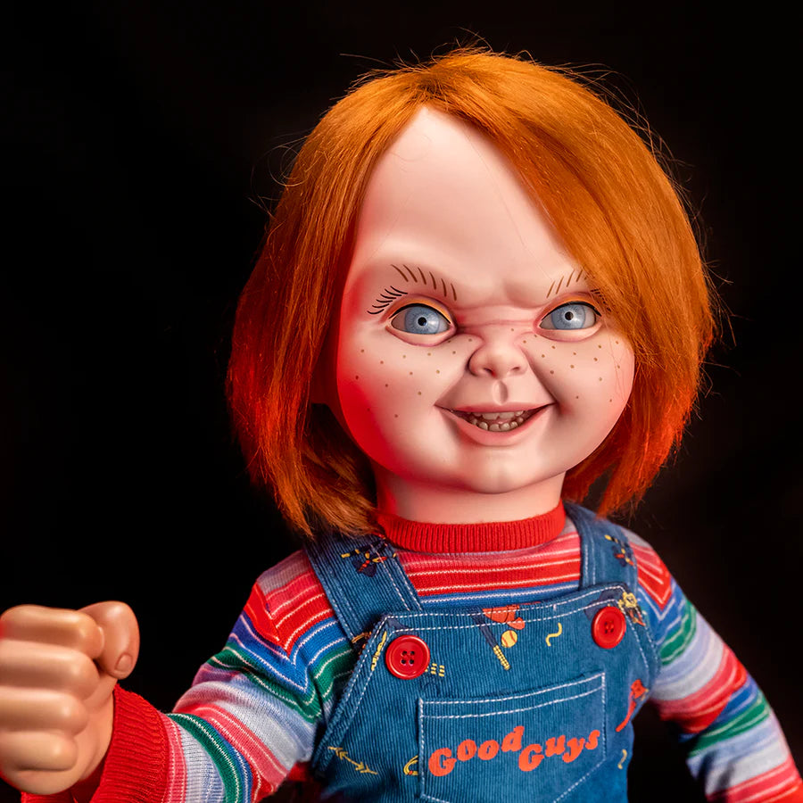 This is a Child's Play 2 Ultimate Chucky doll and he is wearing blue jean overalls, a striped long sleeve shirt, red shoes and he has orange hair, blue eyes and freckles
