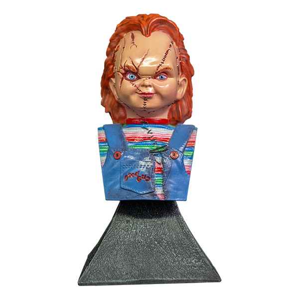 This is a Bride of Chucky mini bust and he has orange hair, a striped shirt, blue overalls and stitches on his face and is on a grey stand.