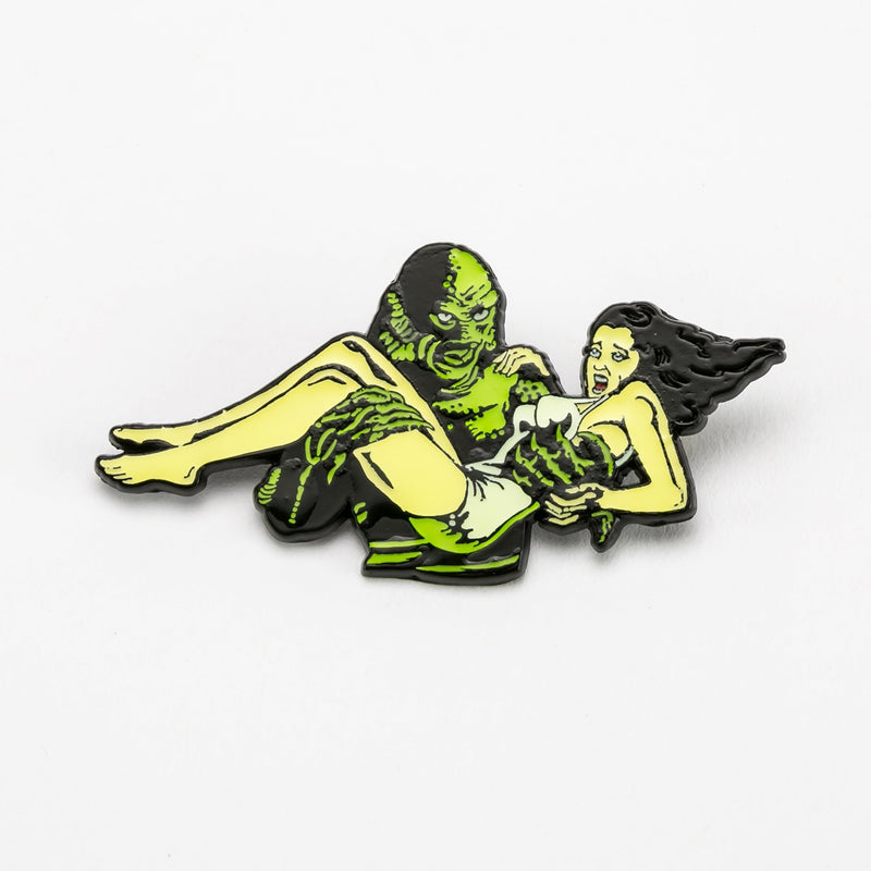 This is a Universal Monsters Creature from the Black Lagoon enamel pin that has a girl with dark hair and a white bathing suit being carried by Creature.