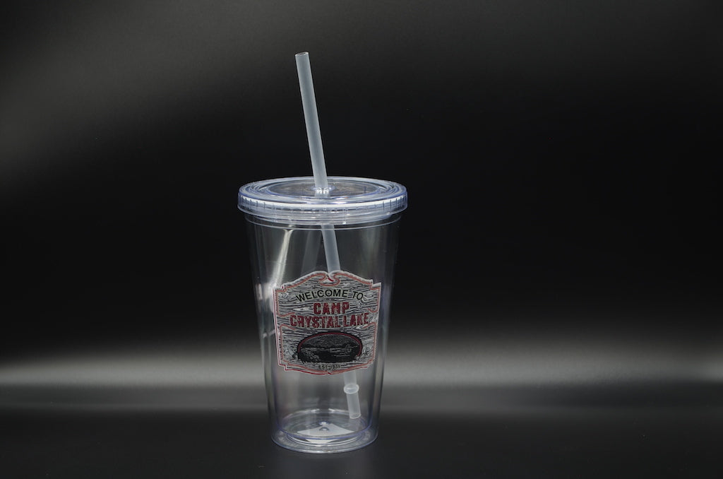 This is a Friday the 13th Camp Crystal Lake cup and straw that has a brown wooden sign with red welcome to letters.