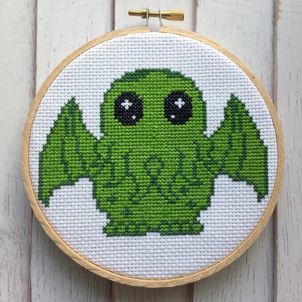 This is a DIY cross stitch kit and has a green Cthulhu and he has black eyes and a wooden hoop.