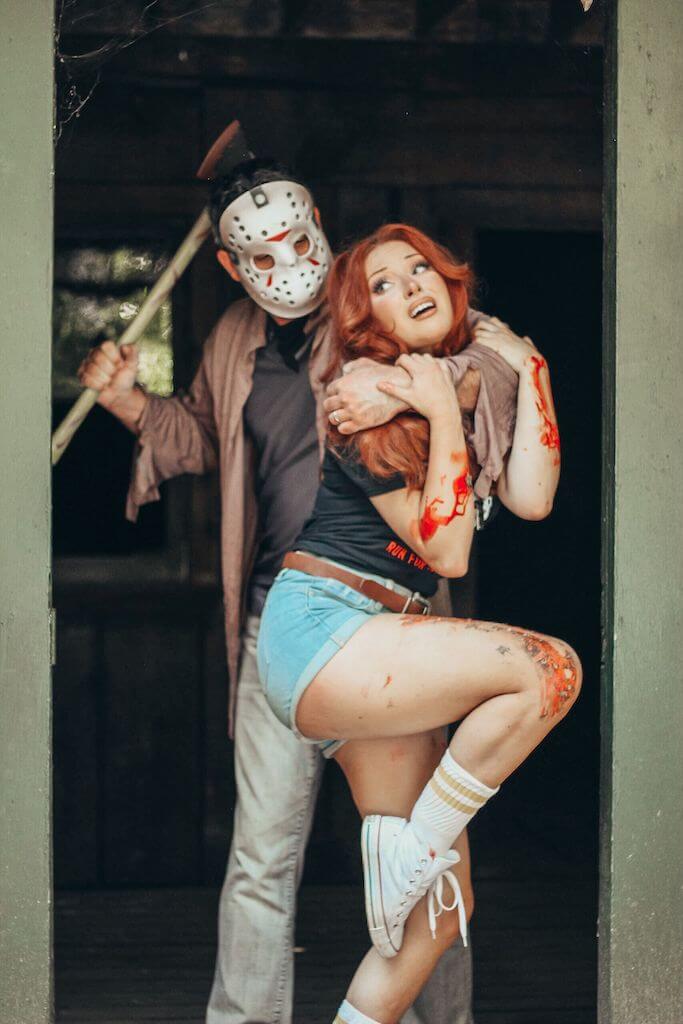 There is a camp counselor with red hair, a black camp crystal lake running team shirt and denim shorts being held, while Jason Voorhees stands behind her in a hockey mask and brown shirt, while holding an axe.
