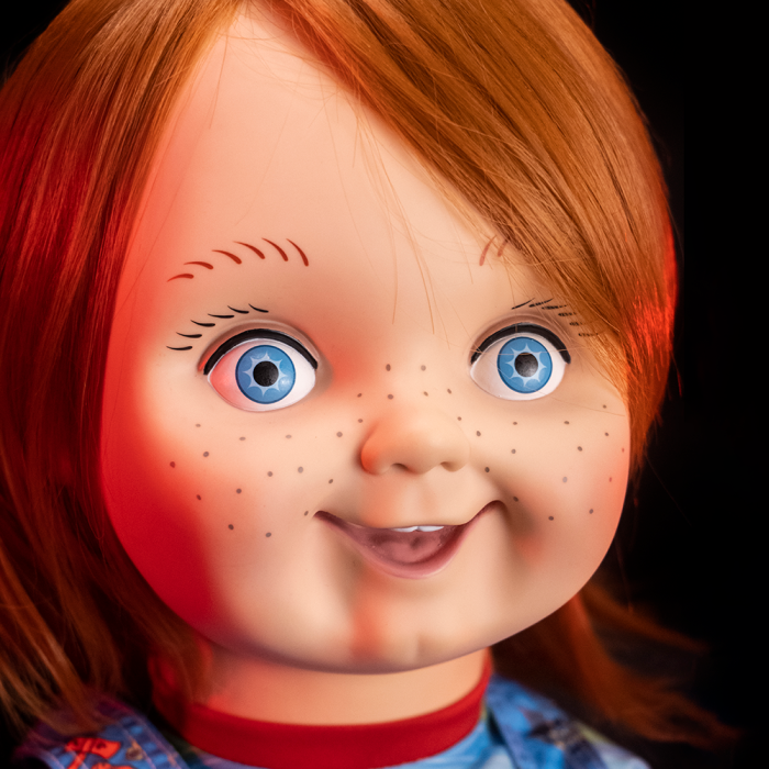 This is a Child's Play Chucky Good Guy doll and he has blue eyes, freckles and orange hair and a red ringed collar..