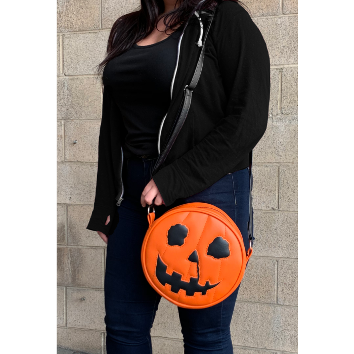 This is a Halloween 1978 pumpkin purse that is orange with a black strap and has black eyes, black nose and an orange smile. and is on someone with jeans and a black sweatshirt.