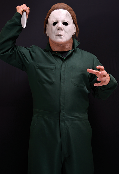 This is a Halloween 2 Michael Myers coverall that is green with pockets and he is wearing a white mask with brown hair and holding a knife.