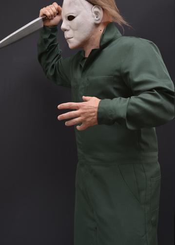 This is a Halloween II Michael Myers coveralls that are green with pockets and he is wearing a white mask with brown hair and holding a knife