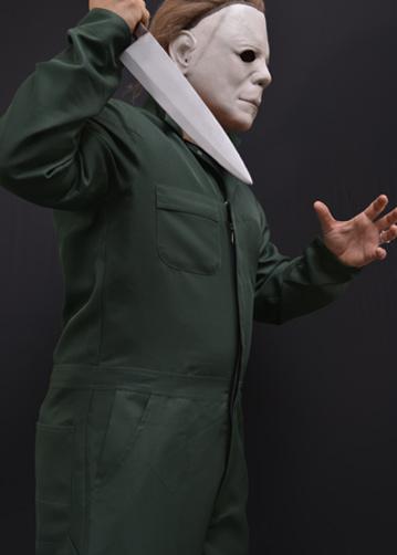This is a Halloween II Michael Myers coveralls that are green with pockets and he is wearing a white mask with brown hair and holding a knife.