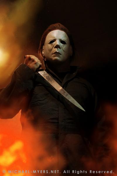 This is a Halloween II Michael Myers mask, that is a white face with brown hair and eye holes, a knife and green coveralls and fire.