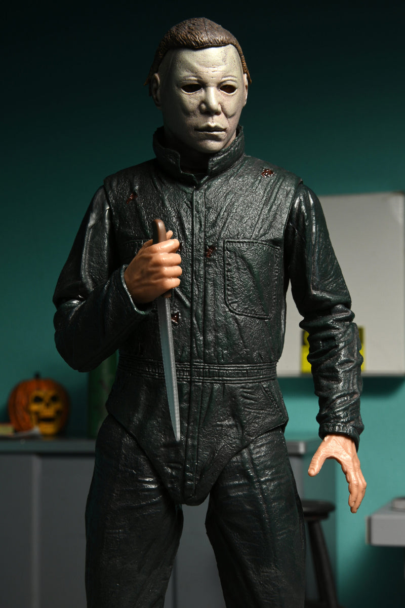 This is a NECA Halloween 2 Michael Myers and Loomis action figure set and Michael has a white mask, brown hair, green coveralls and is holding a silver knife with brown handle, with an orange pumpkin..