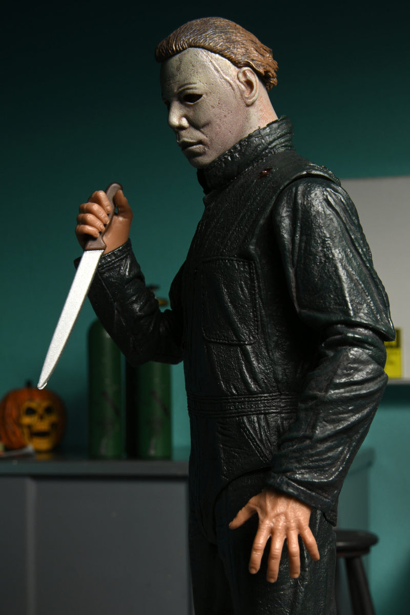 This is a NECA Halloween 2 Michael Myers and Loomis action figure set and Michael has a white mask, brown hair, green coveralls and is holding a silver knife with brown handle.