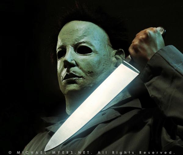 This is a Halloween 6 Curse of Michael Myers mask that is white with brown hair and black eyes and he is wearing coveralls and holding a silver knife.