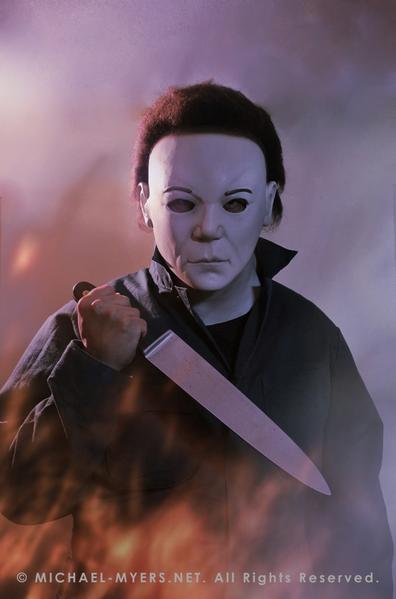 This is a Halloween 8 Resurrection Michael Myers mask that is a white face, brown hair and black eyes with coveralls, a silver and shiny knife, with white smoke and fire.