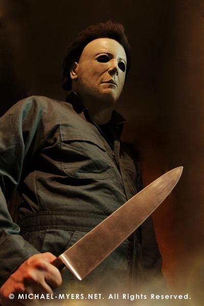 This is a Michael Myers Halloween H20 Mask that is white with brown hair and he is wearing green coveralls and holding a knife in his hand.