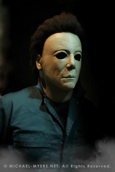 This is a Michael Myers Halloween H20 Mask that is white with brown hair and he is wearing green coveralls.