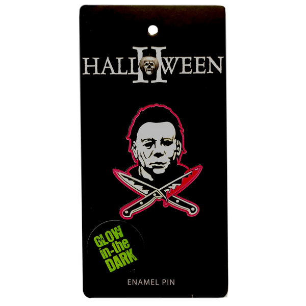 This is a Halloween Michael Myers enamel pin and he has a white mask and there are two bloody knives in front of him.