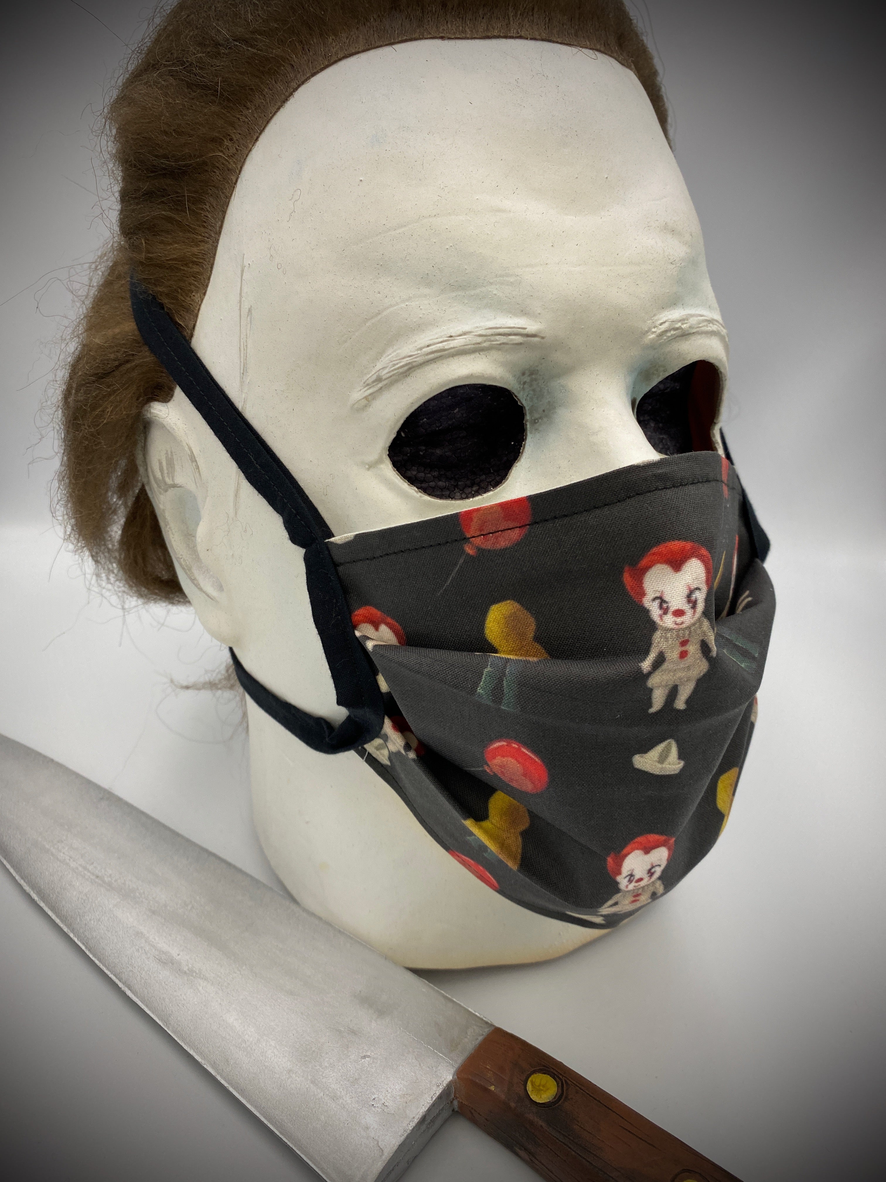 This is a black protective face mask with black ties and it is Pennywise from It 2017 and has white boats, red balloons and Georgie wearing a yellow rain coat, worn by Michael Myers.