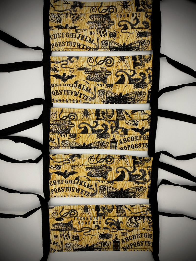This is a brown protective face mask with black ties and it has a ouija board, skeleton, moth, bugs and cages.