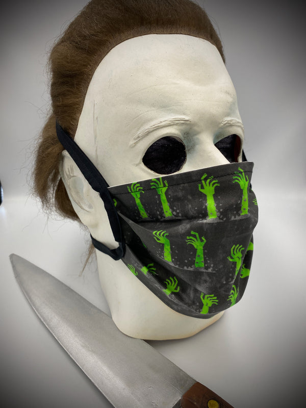 This is a black protective face mask with black ties and it has green zombie arms and hands coming out of the dirt, worn by Michael Myers.
