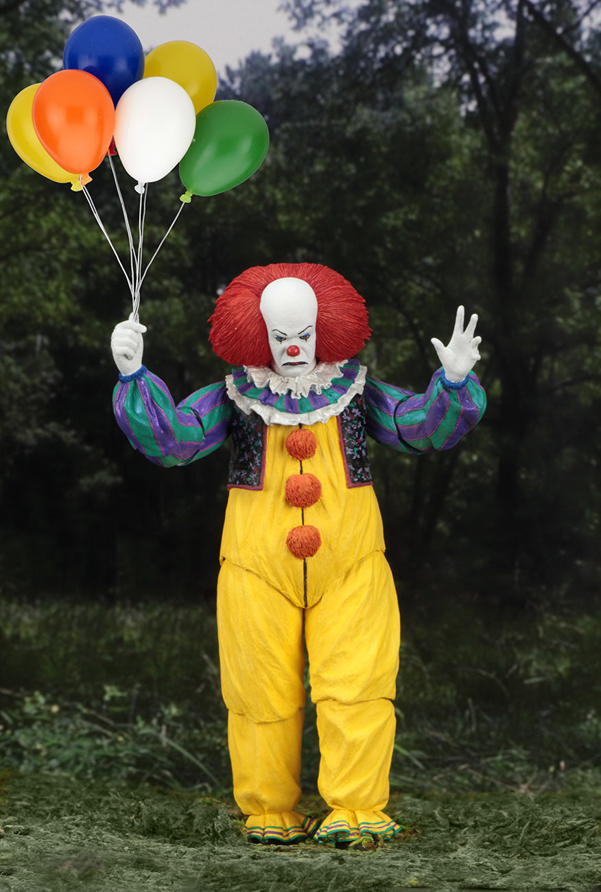 This is an It Movie 1990 NECA ultimate action figure with Pennywise who has a white face, red nose, orange red hair, yellow suit with orange balls and green and purple stripes and he is holding multi colored balloons.