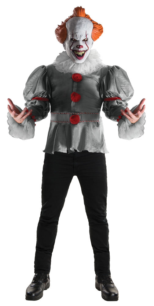Pennywise the clown is standing and wearing a white face with orange hair, a grey clown top with red balls and a white collar. 
