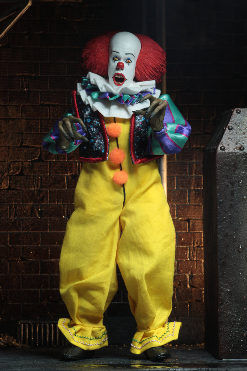 This is an It movie 1990 8' clothed action figure from NECA and Pennywise has a yellow suit with orange balls, purple and green striped sleeves, white face, yellow eyes, orange red hair and claw hands.