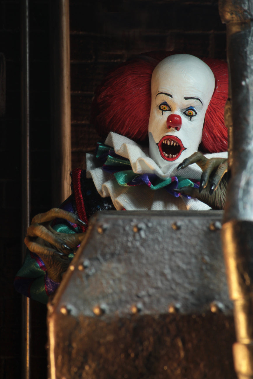 This is an It movie 1990 8' clothed action figure from NECA and Pennywise has a yellow suit with orange balls, purple and green striped sleeves, white face, yellow eyes, orange red hair, claw hands and he looks surprised.