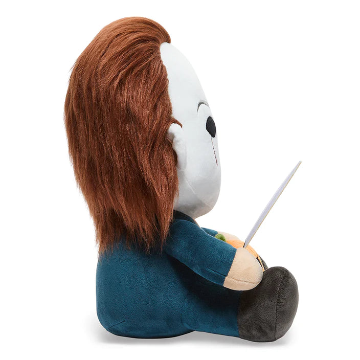 This is a Halloween movie Michael Myers Hugme Kidrobot plush and he has a white mask, brown hair, silver knife, blue coveralls and an orange pumpkin in his lap