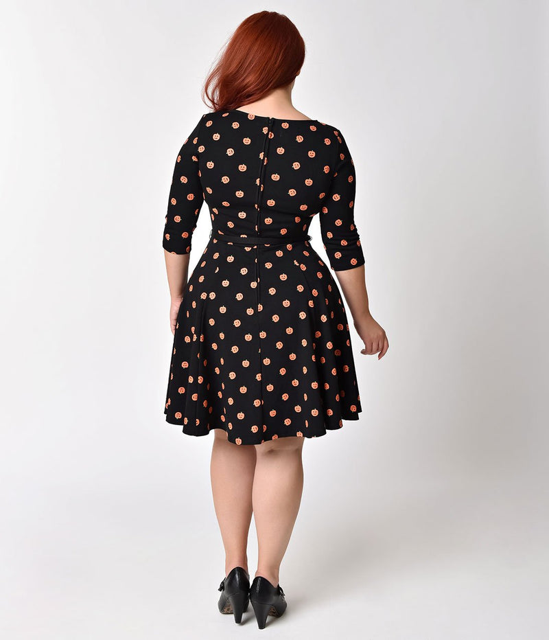 This is a black pinup flare dress with orange pumpkins and 3/4 sleeves, belt and the plus model is wearing black shoes.