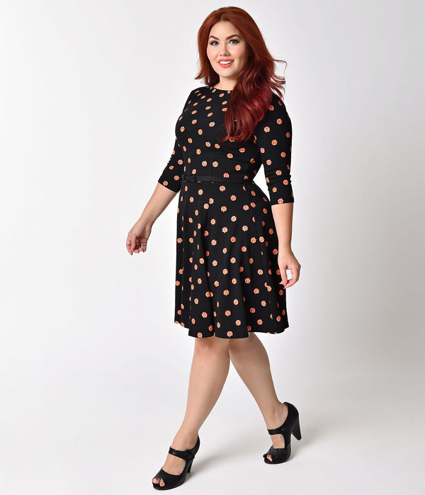 This is a black pinup flare dress with orange pumpkins and 3/4 sleeves and the plus model is wearing black shoes.