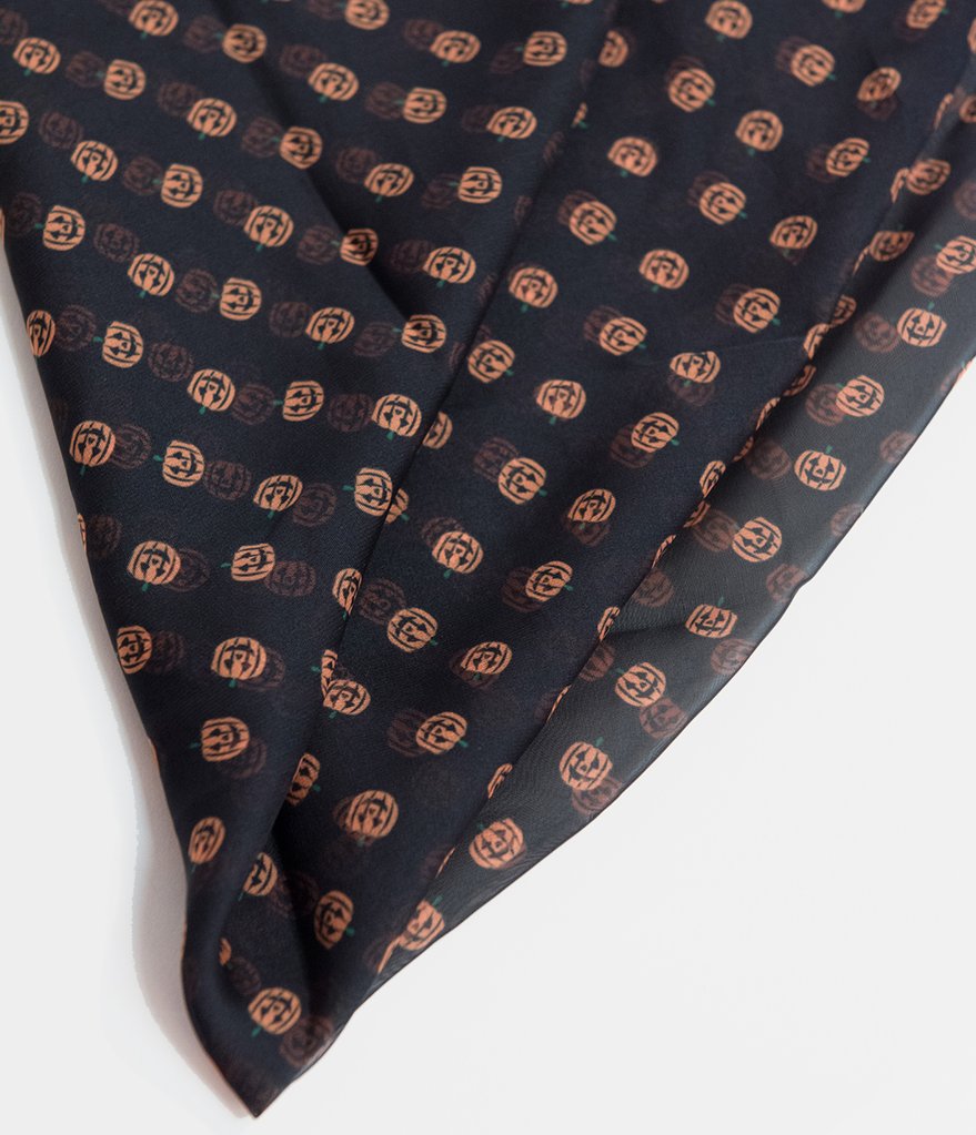 This is a black pinup style chiffon hair scarf that has smiling orange pumpkins on it.