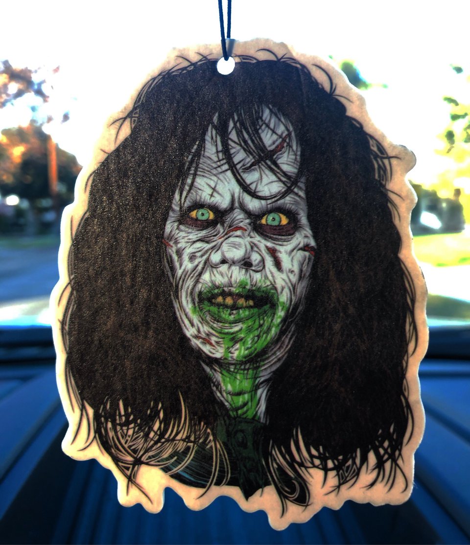 This is a Regan Exorcist air freshener and she has dark hair and green puked vomit on her face.