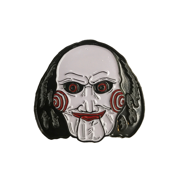 This is a Saw Billy enamel pin from Trick Or Treat and he has a white face, black hair, red lips and eyes and bullseye cheeks.